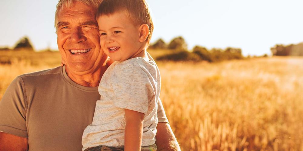 Older man holding a toddler, both smiling.